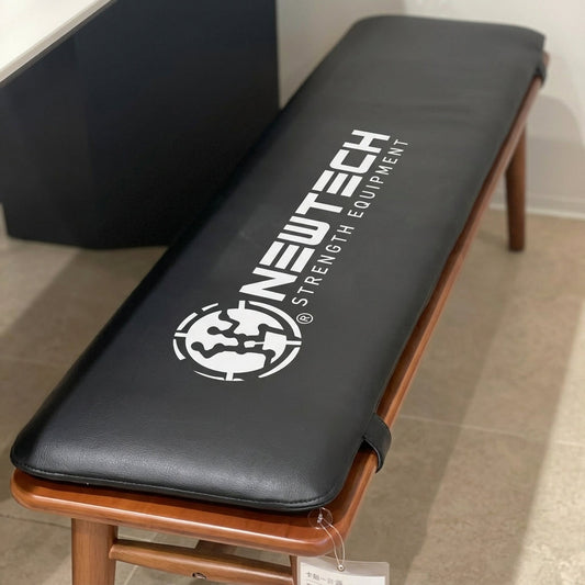 NewTech Strength Equipment branded gym bench cushion with white logo sublimation printed on dark gray fabric on wooden bench