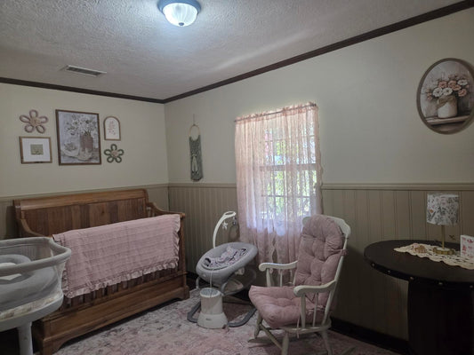 Nursery glider rocker with custom dusty-pink replacement cushions beside a crib and bassinet