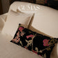 Black floral throw pillow styled on modern sofa with pink and coral blooming flowers
