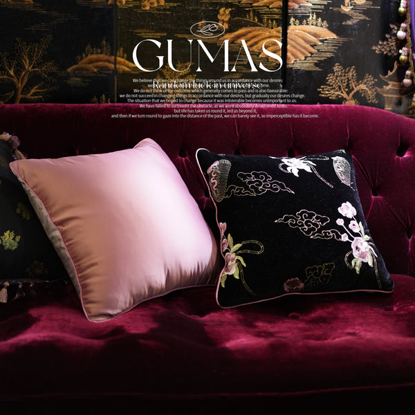 Black velvet throw pillow with white crane and pink peony embroidery next to solid pink velvet pillow on burgundy sofa