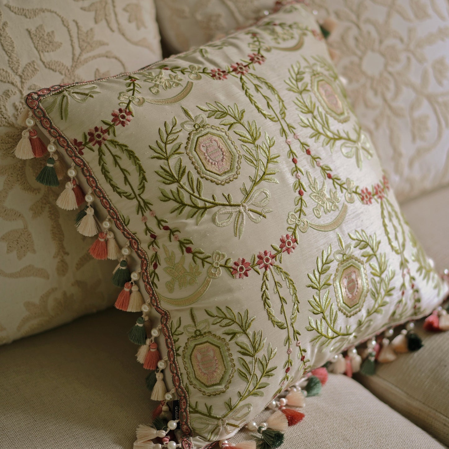 Close-up of hand-embroidered hexagonal medallion with pink roses and sage green laurel wreath on cream linen pillow